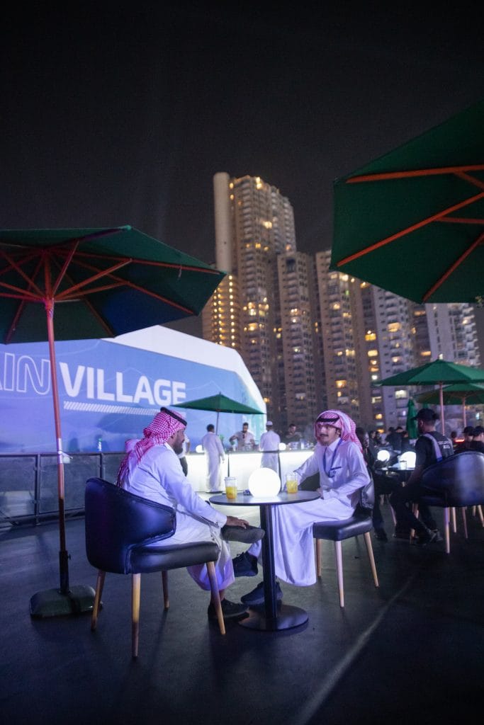 Guests at a lit bar on a rooftop lounge beside the Formula 1 fan village